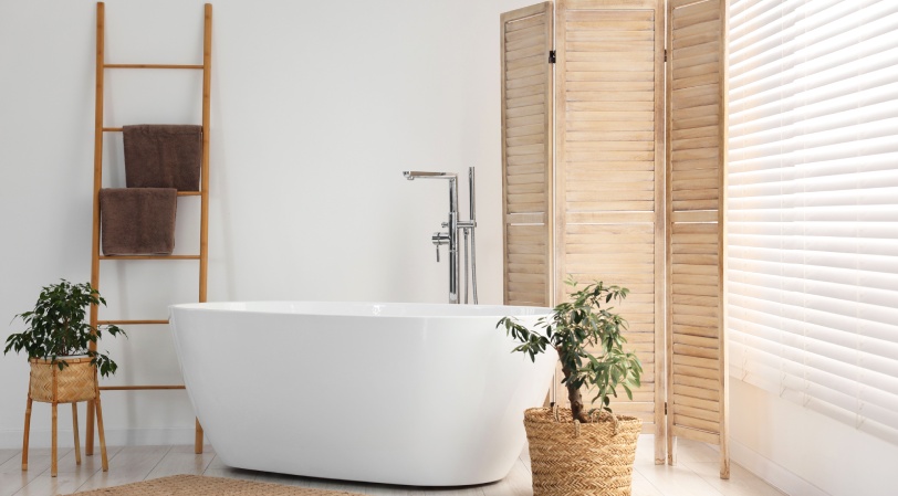 Wooden folding screen, bathtub and green houseplants in bathroom